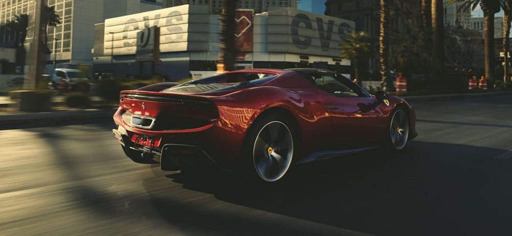A shiny red Ferrari sports car speeds down a city street, palm trees lining the road, under bright daylight, conveying speed and luxury.