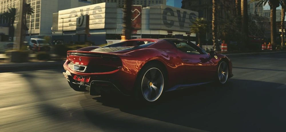 A shiny red Ferrari sports car speeds down a city street, palm trees lining the road, under bright daylight, conveying speed and luxury.