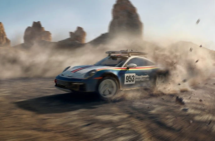 Blue sports car kicking up dust while driving fast across a desert dirt track beneath rocky outcrops
