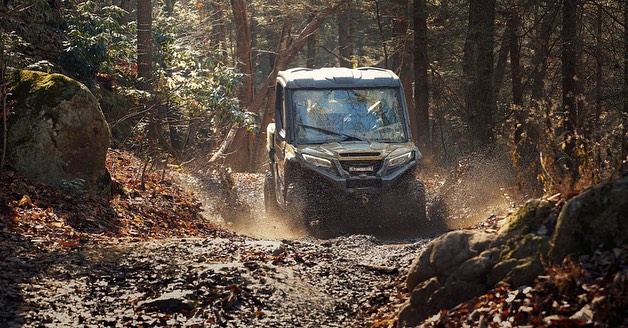 Off-road vehicle splashes through a muddy path surrounded by trees in a forest setting, showcasing outdoor adventure and automotive capabilities.