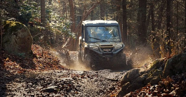 Off-road vehicle splashes through a muddy path surrounded by trees in a forest setting, showcasing outdoor adventure and automotive capabilities.