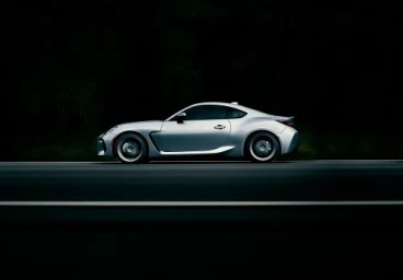 Silver sports car driving along a dark asphalt road at night captured from a low side angle by photographer Dana Neibert.