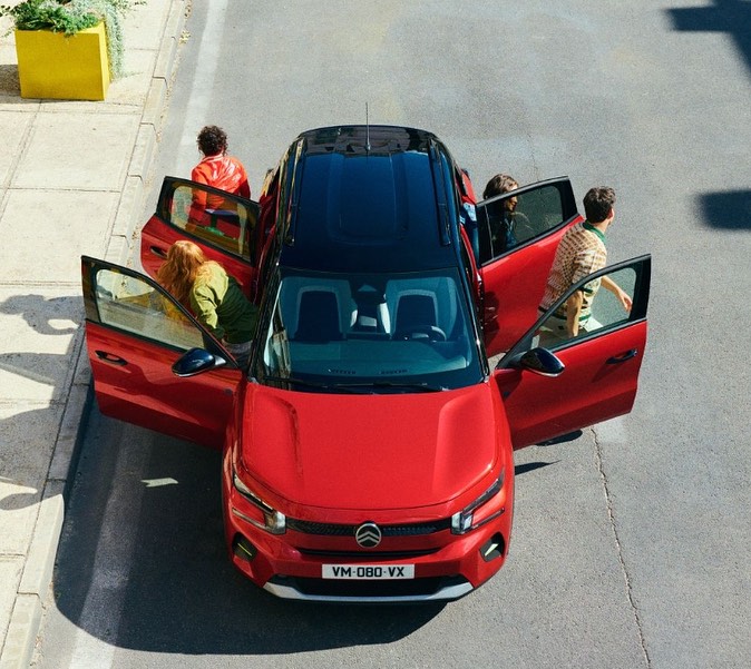 Overhead shot of a red Citroen C3 Aircross SUV with people getting in and out. The car has a black roof and is parked on a city street.