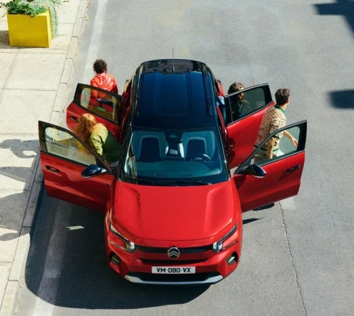 Overhead shot of a red Citroen C3 Aircross SUV with people getting in and out. The car has a black roof and is parked on a city street.