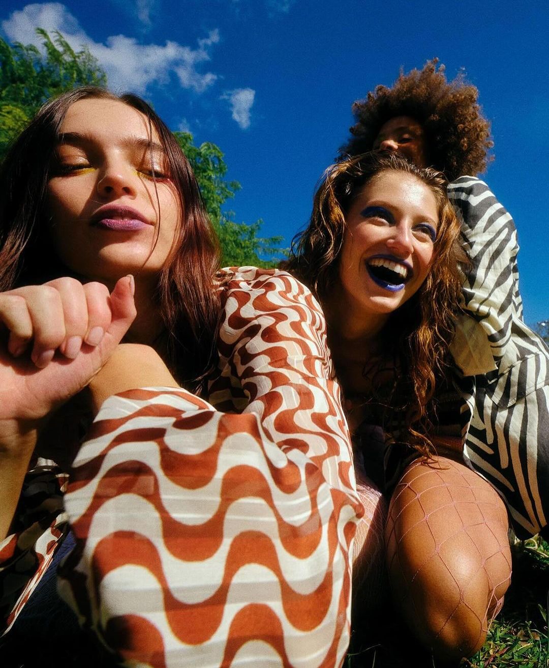 Three young women outdoors under a bright blue sky, photographed from a low angle by Dave Hill.