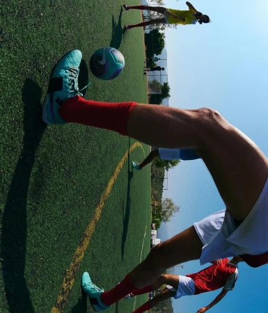 Action shot of a soccer player kicking a ball on a green field, other players in the background, clear sky. Motion and outdoor sport.