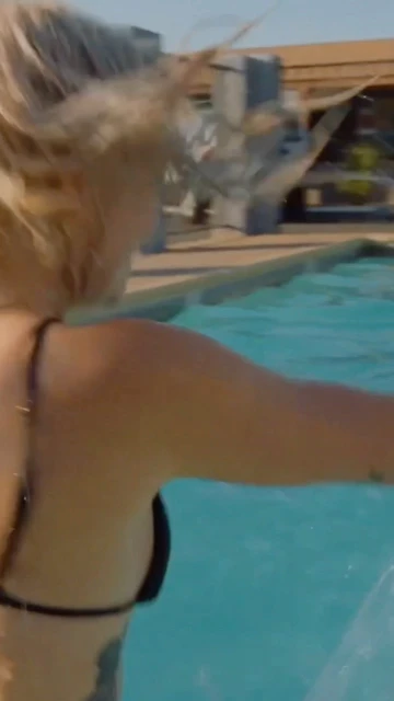 Woman in a black bikini swims in an outdoor pool on a sunny day. Water is splashing as she moves through the clear water.