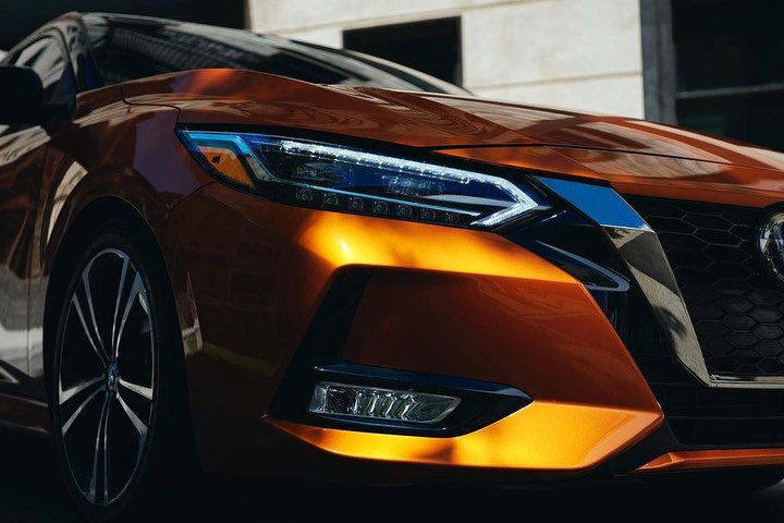 Close-up of a copper Nissan Sentra showcases its sleek headlights, front bumper, and stylish wheel. Modern automotive design.