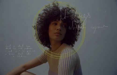 Portrait of a black woman with an afro, wearing a gray top, posing in a photo studio against a dark gray background.