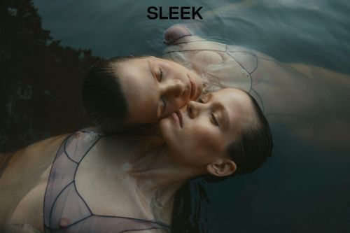 Portrait of two women in water. The women are laying close together with their eyes closed. Moody editorial fashion photograph.