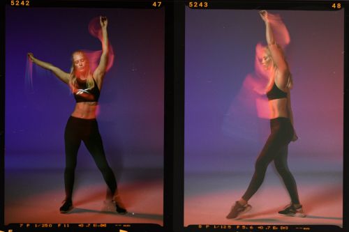 Athletic woman in fitness apparel performs dynamic stretches against a vibrant blue and red background in a dynamic athletic shot.