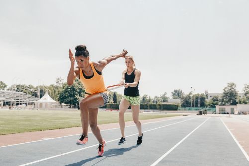Two female athletes training on an outdoor running track with a resistance band, photographed by David Daub.