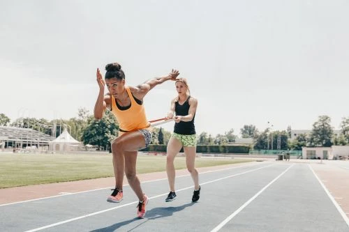 Two female athletes training on an outdoor running track with a resistance band, photographed by David Daub.
