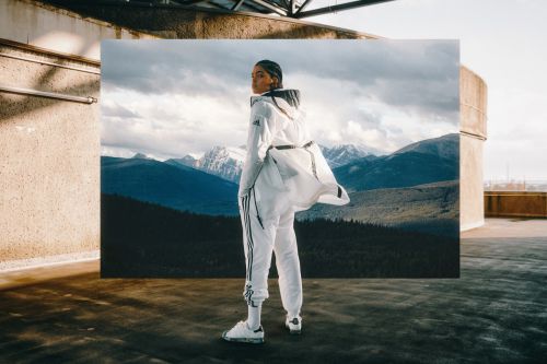 A woman in a white tracksuit stands on a rooftop with a backdrop of mountains in an Adidas fashion editorial shoot, styled with athletic clothing and sneakers.
