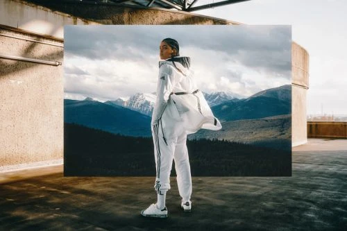 A woman in a white tracksuit stands on a rooftop with a backdrop of mountains in an Adidas fashion editorial shoot, styled with athletic clothing and sneakers.