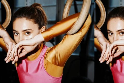 Close-up studio shot of a young adult female athlete with her hands on gymnastic rings, wearing pink and gold athletic wear.