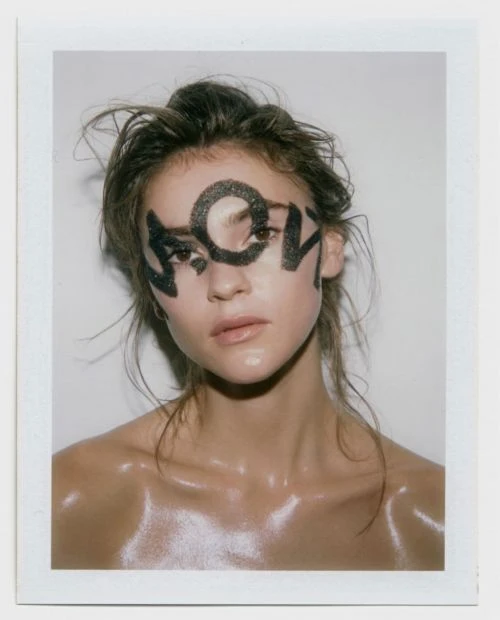 Close-up portrait of a young adult woman with artistic makeup around the eyes, set against a plain white backdrop in a studio setting.