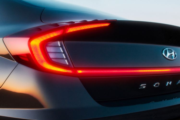 Close-up of a dark blue Hyundai Sonata's rear with illuminated taillights. Automotive design with sleek lines and manufacturer's logo.