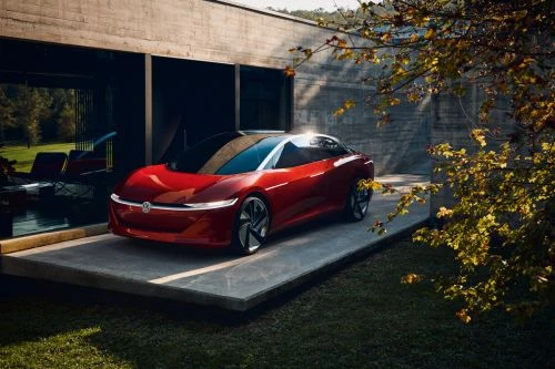 A red Volkswagen ID.AERO electric car parked on a concrete platform outside a modern building with green foliage in the background.