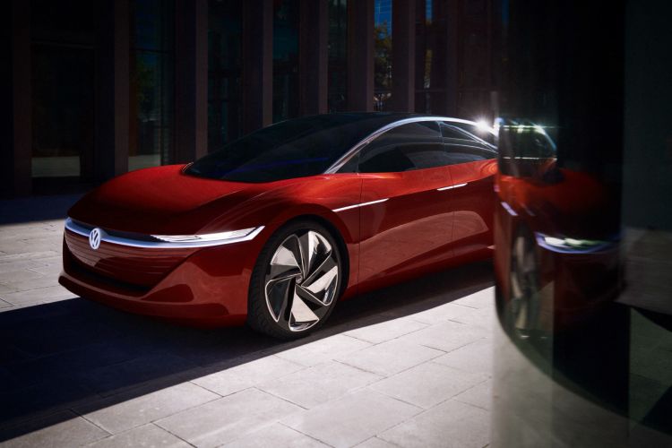 Red Volkswagen electric car on a paved surface outside a modern building with large windows and sunlit shadows, automotive design.