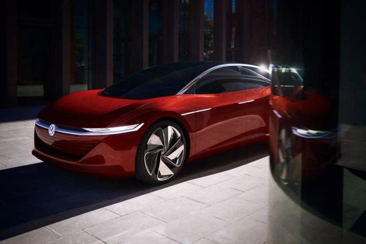 Red Volkswagen electric car on a paved surface outside a modern building with large windows and sunlit shadows, automotive design.