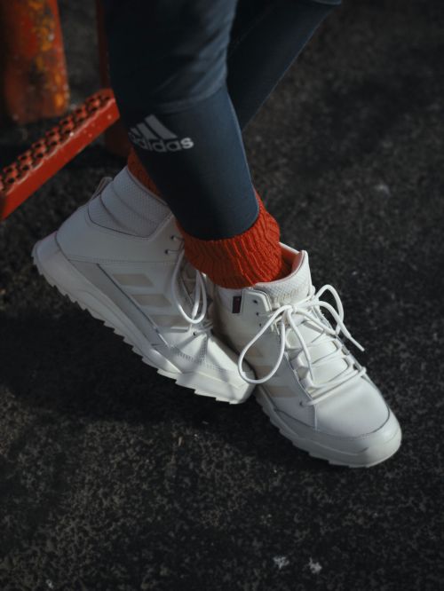 Close-up shot of white Adidas high-top sneakers worn with red socks and black athletic pants showing the brand's logo.