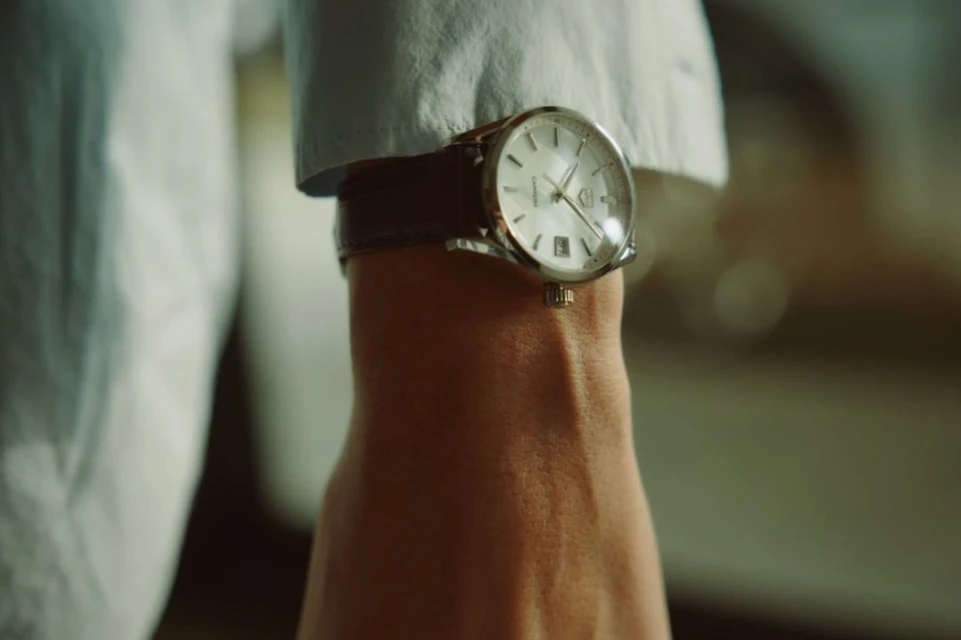 Wrist shot of a man wearing a silver wristwatch with a leather strap and white shirt, focusing on the wristwatch details.