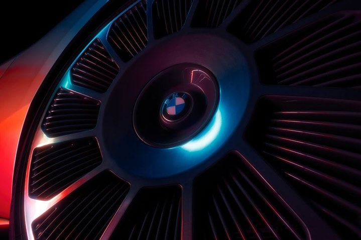Close-up of a BMW wheel featuring a distinctive design with a central logo, enhanced by blue and red lighting against a dark backdrop.