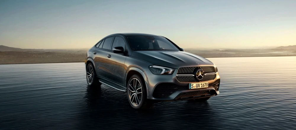 Silver Mercedes GLE Coupe on a reflective surface with a scenic backdrop of rolling hills and an endless pool at dusk.