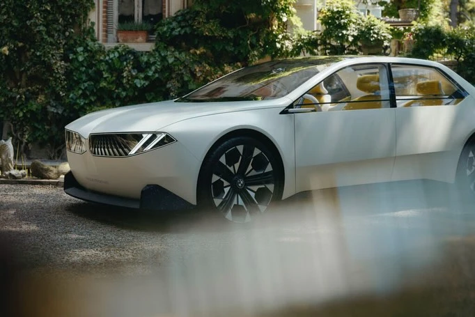 Sleek white BMW concept car parked outside a stone building with green leafy vines on the exterior walls, illuminated by natural light.