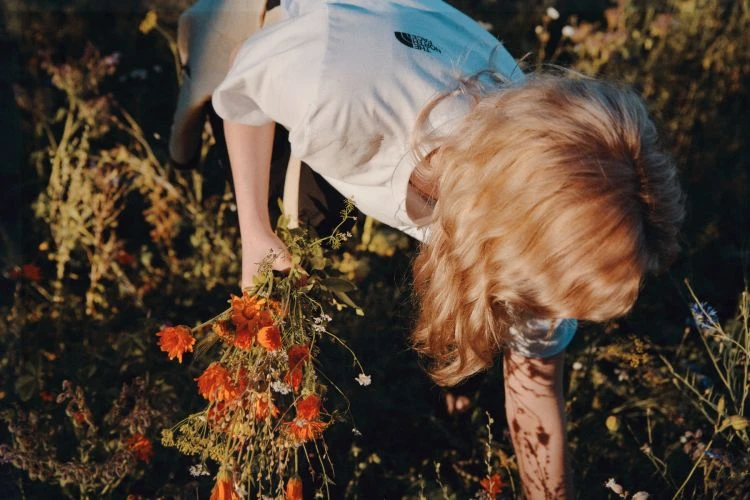 Young woman picking flowers in a field. She is wearing a white t-shirt and the flowers she is holding are orange and white.