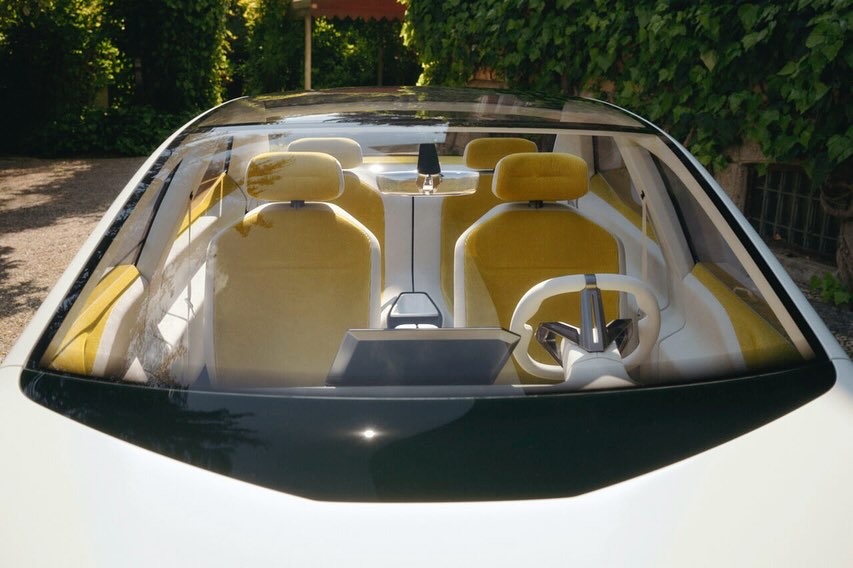 Front view of a modern car interior featuring yellow seats, a white steering wheel, and a sleek dashboard under a glass roof.