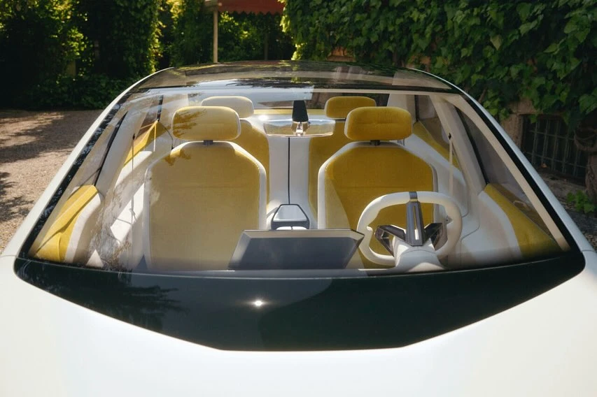 Front view of a modern car interior featuring yellow seats, a white steering wheel, and a sleek dashboard under a glass roof.
