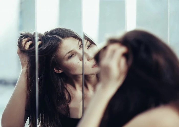 Woman reflected in vertically segmented mirror panels touching her long dark hair