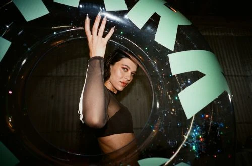 A woman poses inside of a transparent inflatable tube with green arrow graphics, featuring an indoor setting and dark background.
