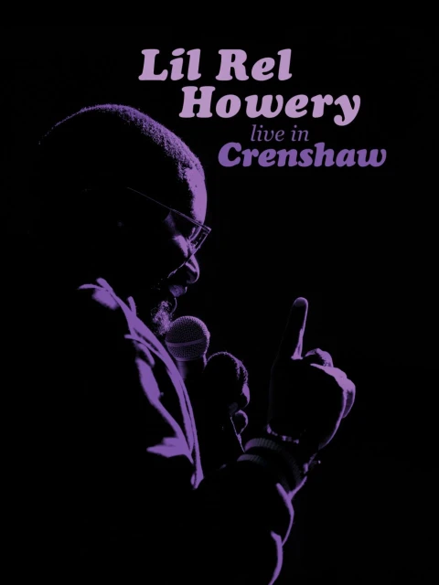 Silhouette of Lil Rel Howery on stage with a microphone, finger raised, bathed in violet light against a dark background.