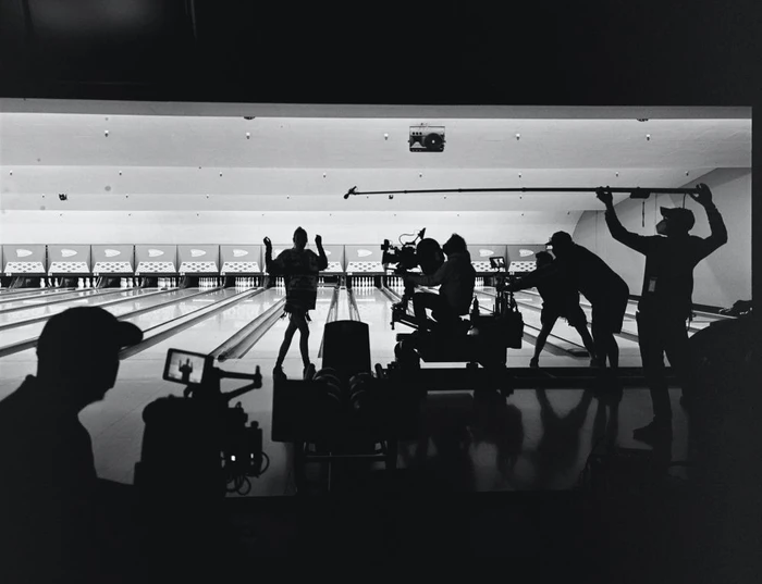 Behind-the-scenes shot of a film crew silhouetted inside a bowling alley during a production shoot.