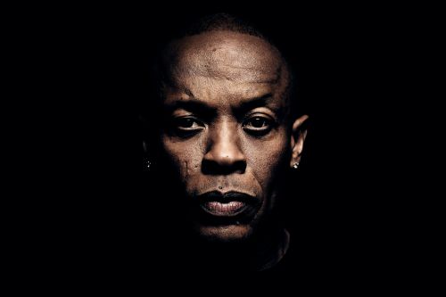 Close-up portrait of an African-American adult male with dark lips and short hair, set against a stark black background.