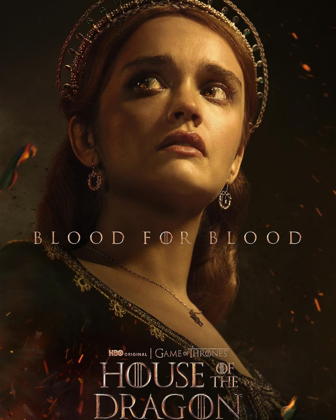 Close-up portrait of a young adult female wearing a crown, ornate earrings, and necklace in a dark, moody scene for TV show 'House of the Dragon'.