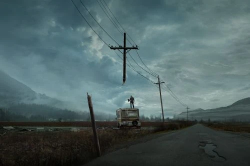 A man stands atop a vintage camper in a desolate landscape under a cloudy sky, next to an empty road and powerlines with mountains in the distance.