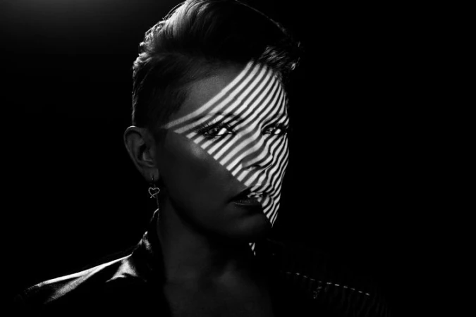 Striking black and white portrait of a woman with short hair, featuring a pattern of light projected across her face in a dark setting.