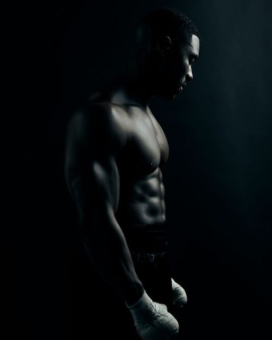 Muscular African-American man with bare chest and boxing wraps, low key lighting, dramatic shadows in a dark studio setting.