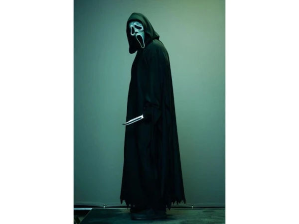 Person in Scream Ghostface mask and black robe, holding a knife, stands in profile against a green backdrop. Horror film concept.