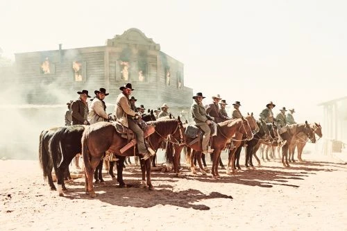Group of cowboys on horseback in a Western town setting with a building appearing to be on fire, creating a dramatic scene.