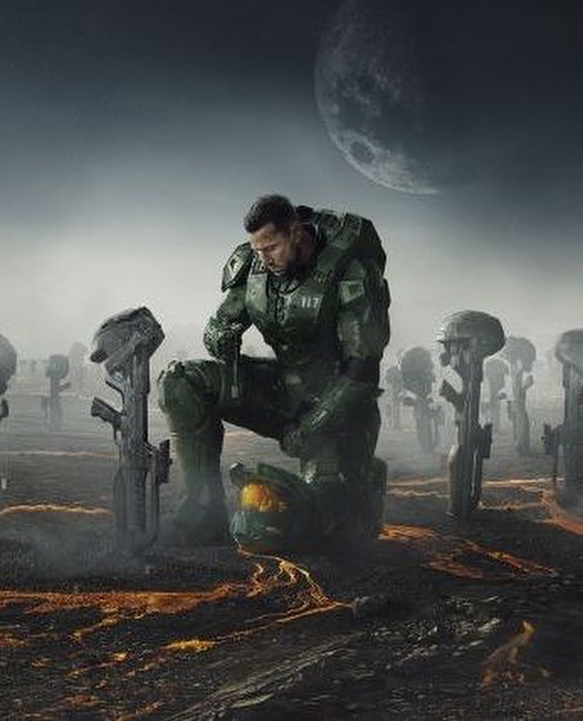 Man in futuristic armor kneels among fallen helmets and rifles in a solemn, desaturated outdoor scene with a large moon in the sky.