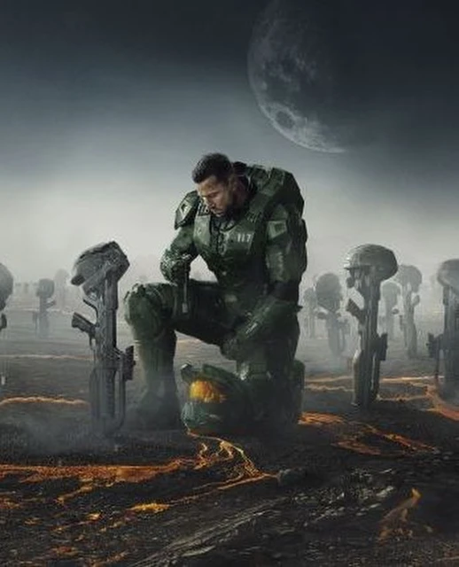 Man in futuristic armor kneels among fallen helmets and rifles in a solemn, desaturated outdoor scene with a large moon in the sky.