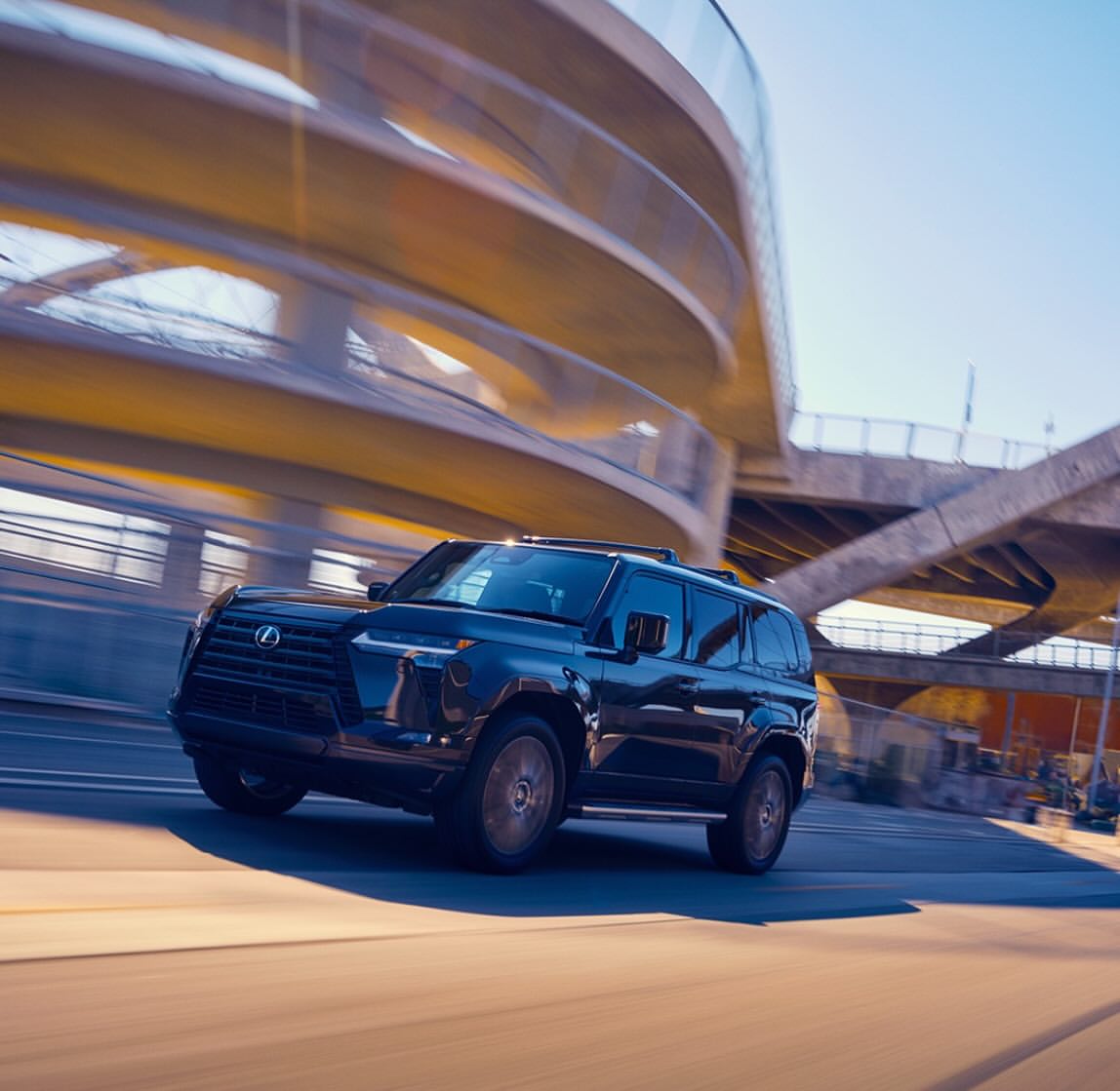 Luxury black SUV driving on an asphalt road with an urban overpass in the background, motion blur conveys speed and automotive prowess.