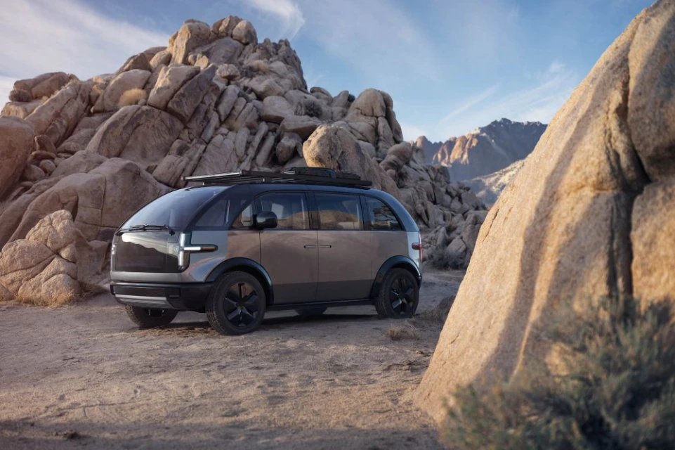Modern electric car parked on a sandy plain surrounded by rock formations and mountains against a blue sky. Vehicle for automotive industry.