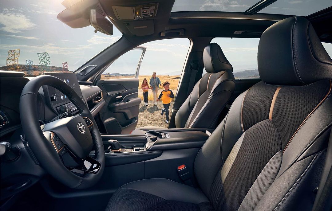 Car interior with leather seats; an adult female, a boy, and a girl walk away from the vehicle in a desert landscape with a blue sky.