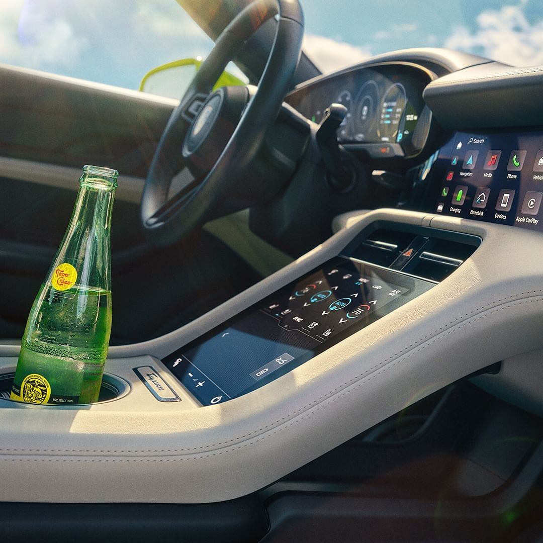 Car interior with a glass bottle of sparkling water in the cupholder of a car's center console with a digital display and steering wheel.